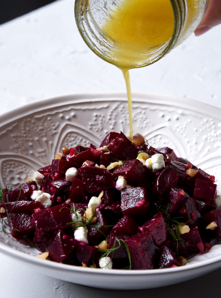 beet salad in a white bowl with simple citrus dressing being poured on top