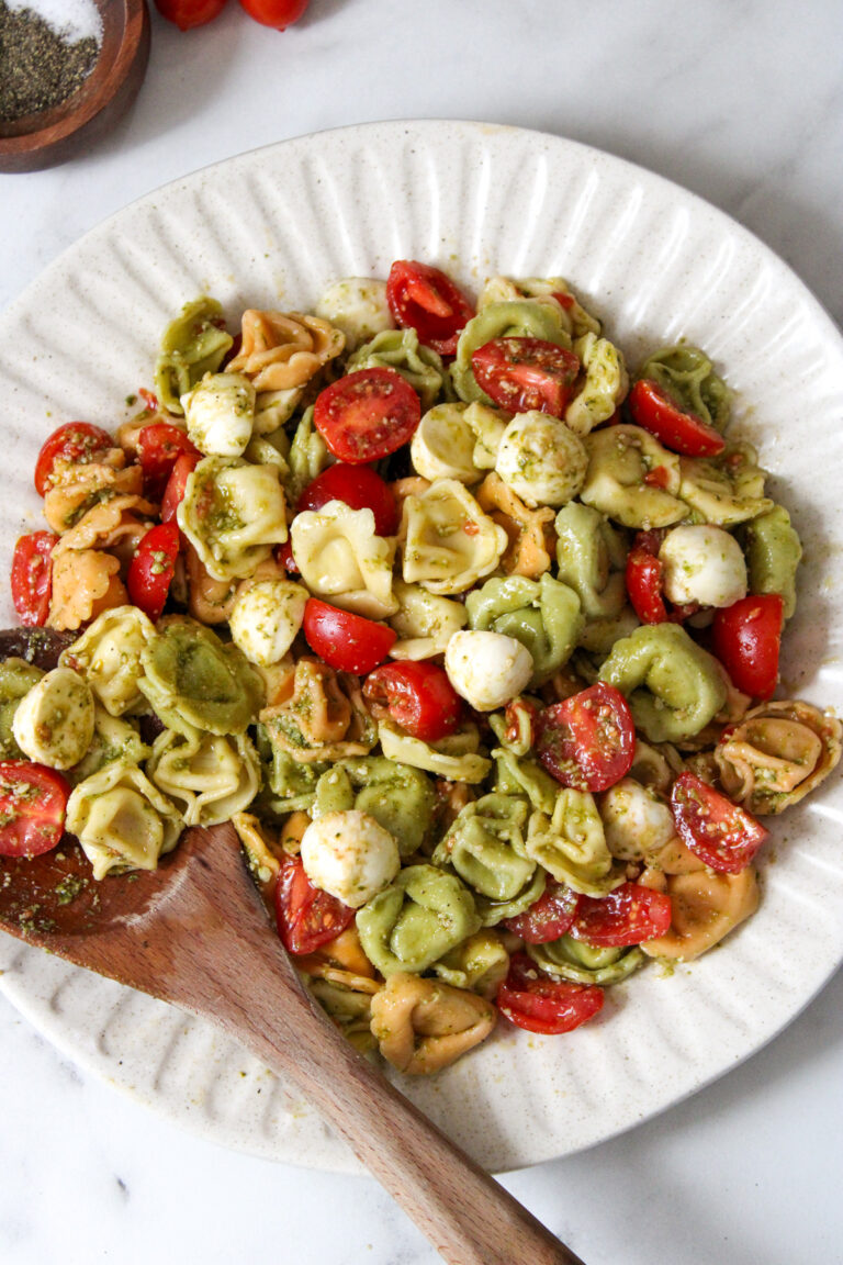 multi-colored tortellini with cherry tomato and fresh mozzarella balls on a white plate with a wooden spoon