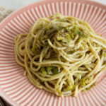 a pink plate holding a mound of spaghetti with caramelized leeks