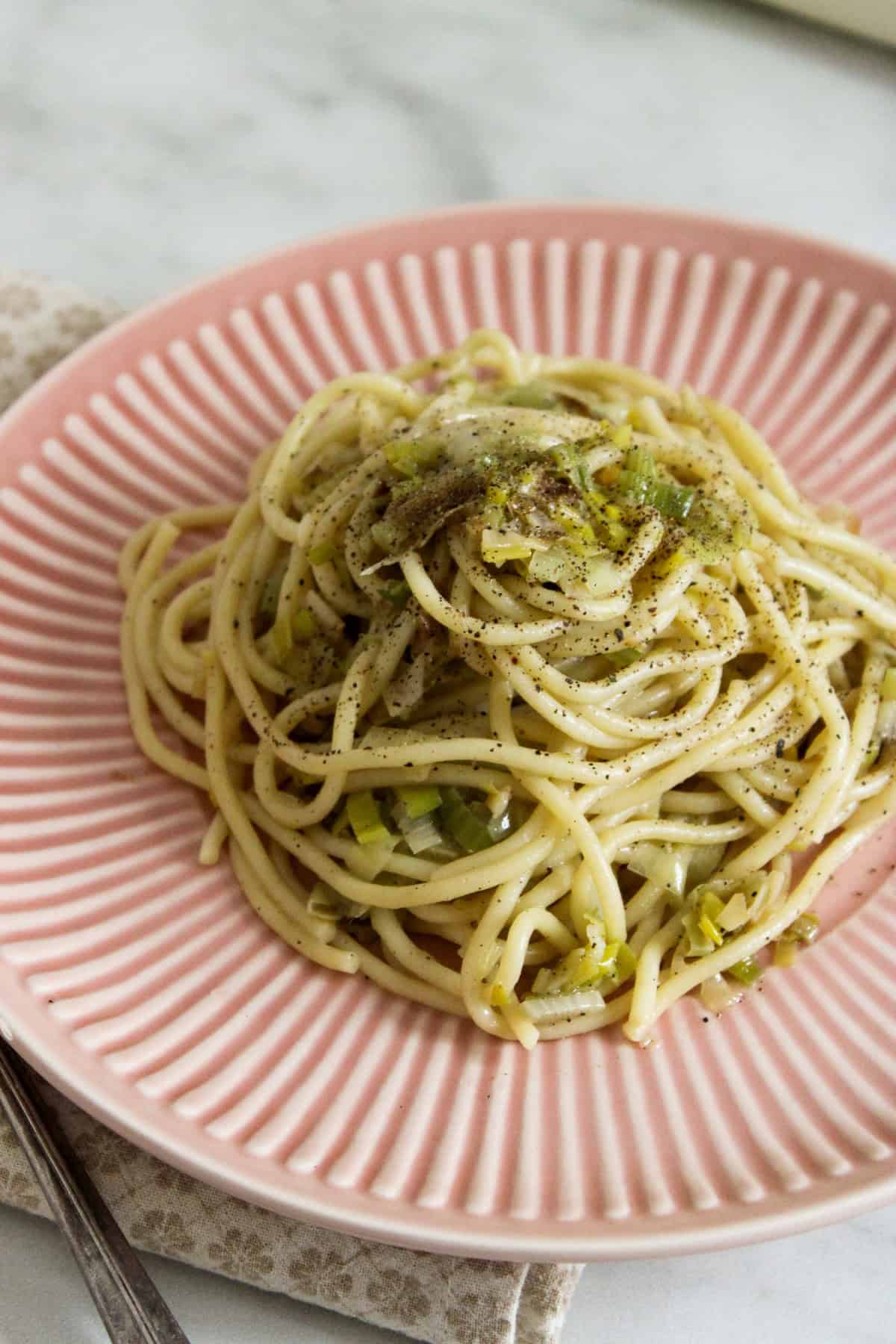 a pink plate holding a mound of spaghetti with caramelized leeks