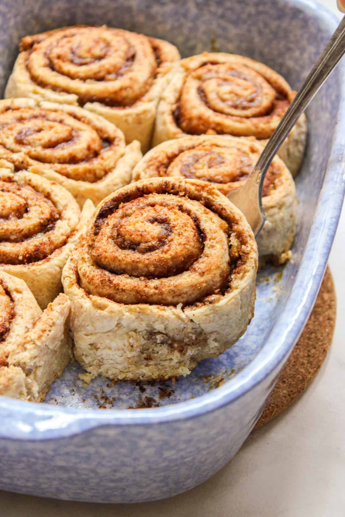 lifting a cinnamon roll out of the baking dish with a metal fork