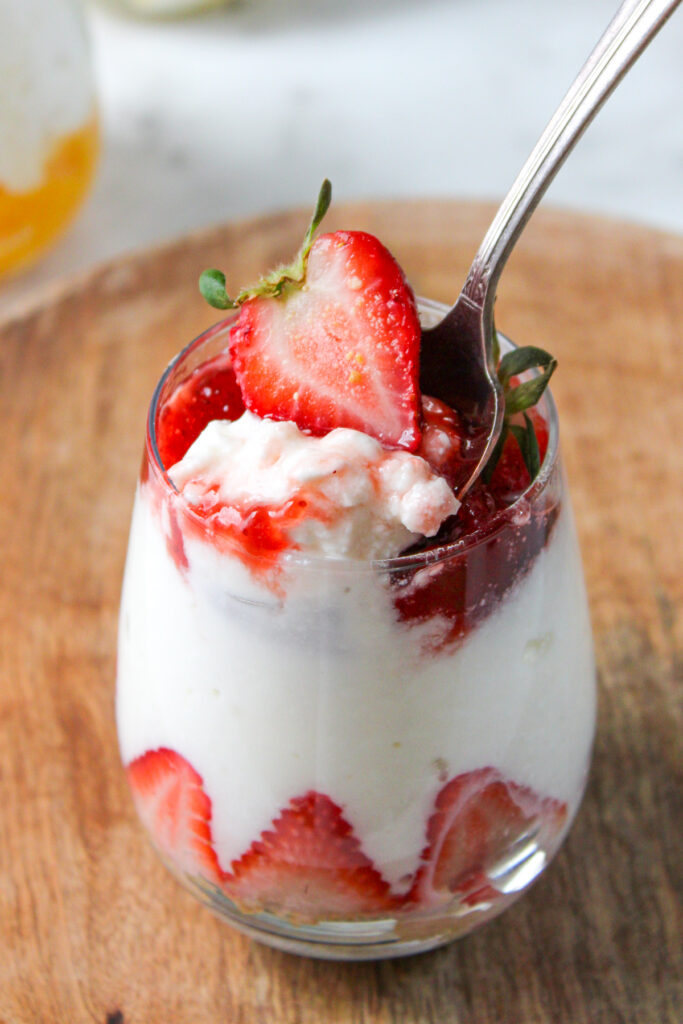 strawberry cottage cheesecake parfait in a small glass cup topped with a fresh strawberry with a spoon digging in