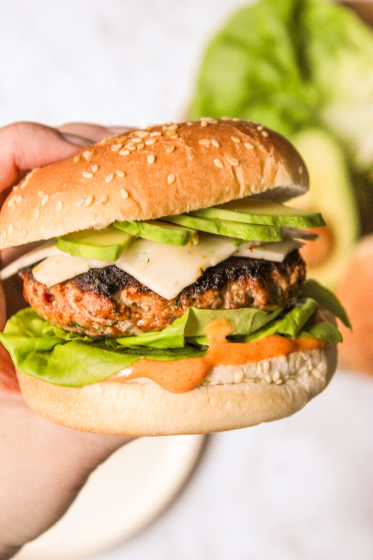 hand grabbing a chipotle turkey smash burger, topped with cheese and sliced avocado. Chipotle aioli is dripping off the bottom bun.