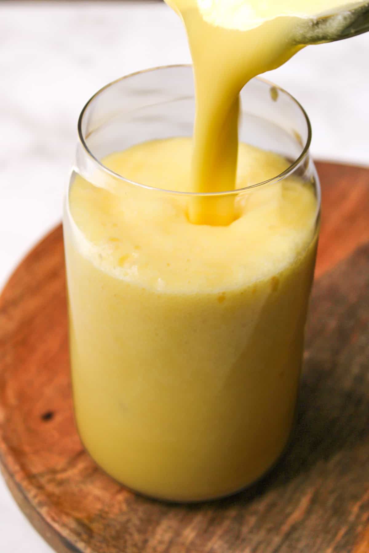 pina colada being poured into a tall glass on a wooden board