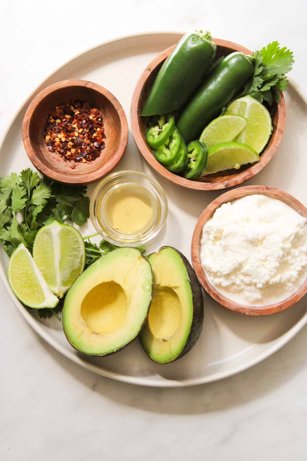 avocado pizza toppings in small wooden and glass bowls arranged on a white plate