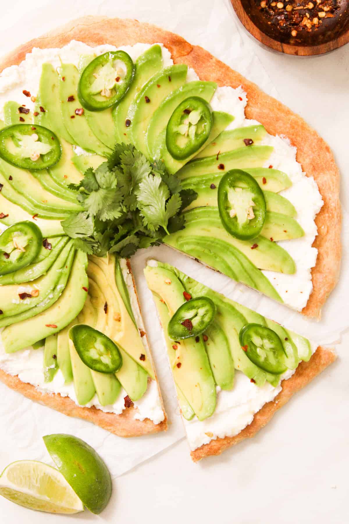 overshot of avocado pizza with a slice cut out 