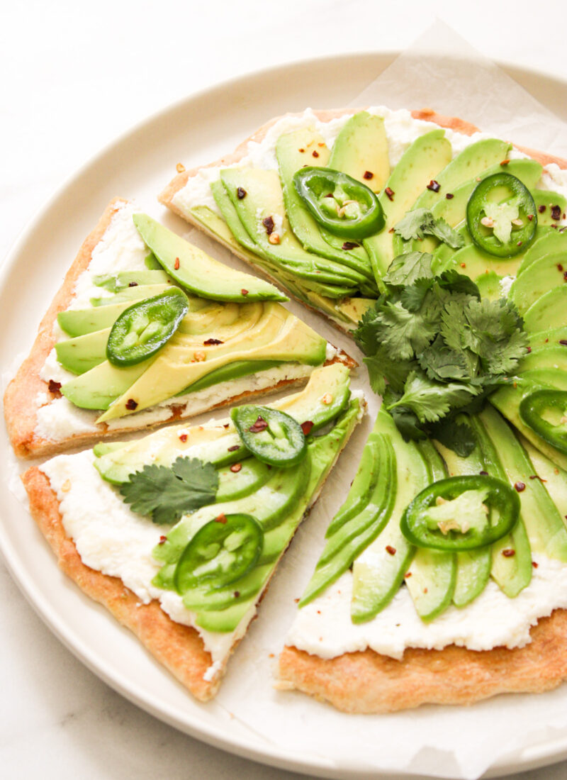 pizza topped with ricotta, fanned avocado, jalapeno and a bundle of cilantro on a white plate