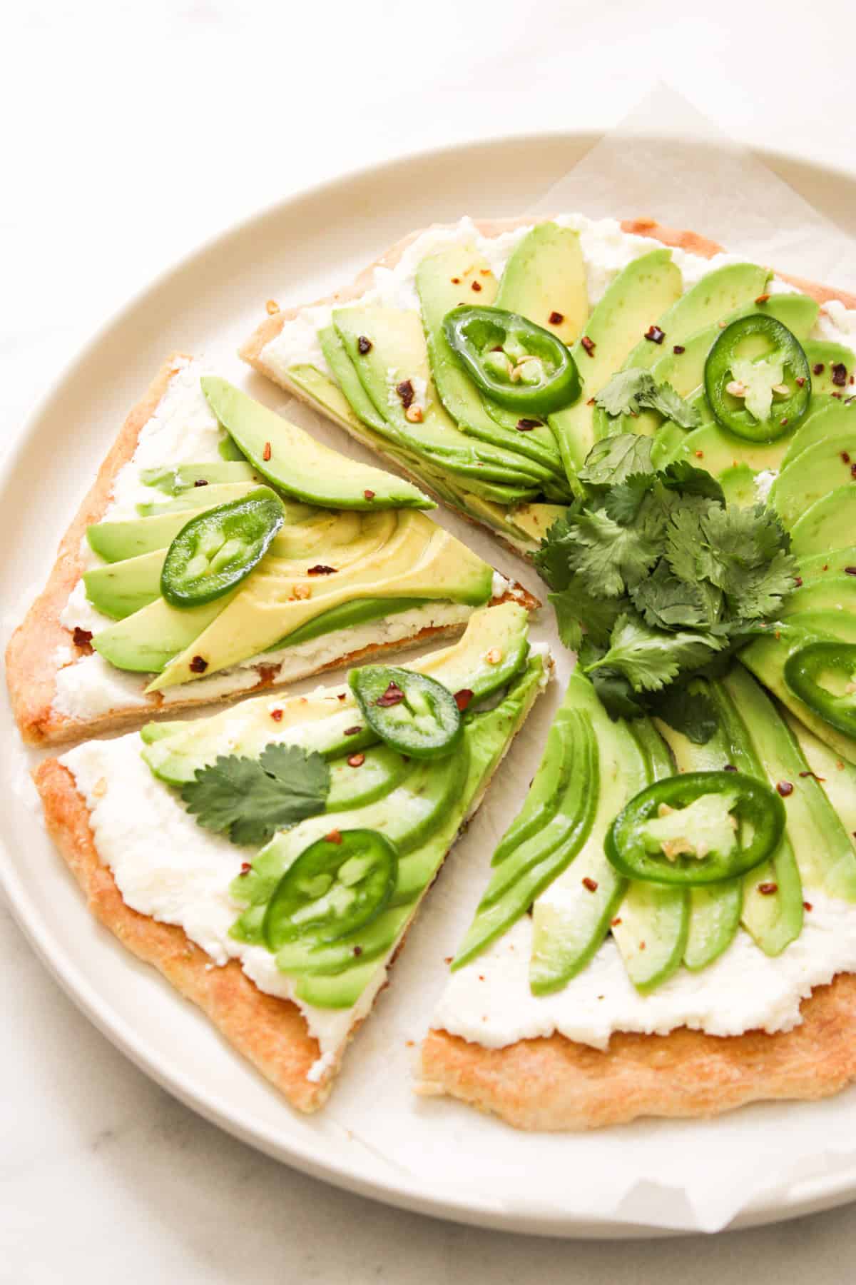 pizza topped with ricotta, fanned avocado, jalapeno and a bundle of cilantro on a white plate