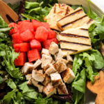 salad in a ceramic bowl topped with cubes of watermelon and chicken, and grilled halloumi cheese