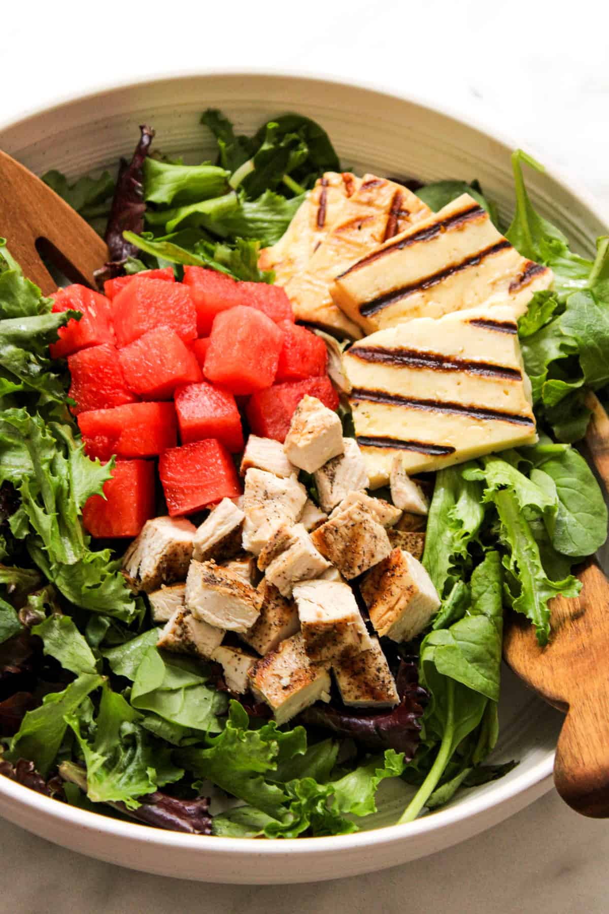 salad in a ceramic bowl topped with cubes of watermelon and chicken, and grilled halloumi cheese