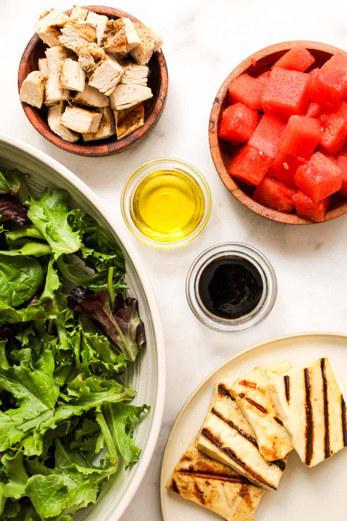 overhead shot of salad ingredients in small glass and wooden bowls arranged on a white marble countertop