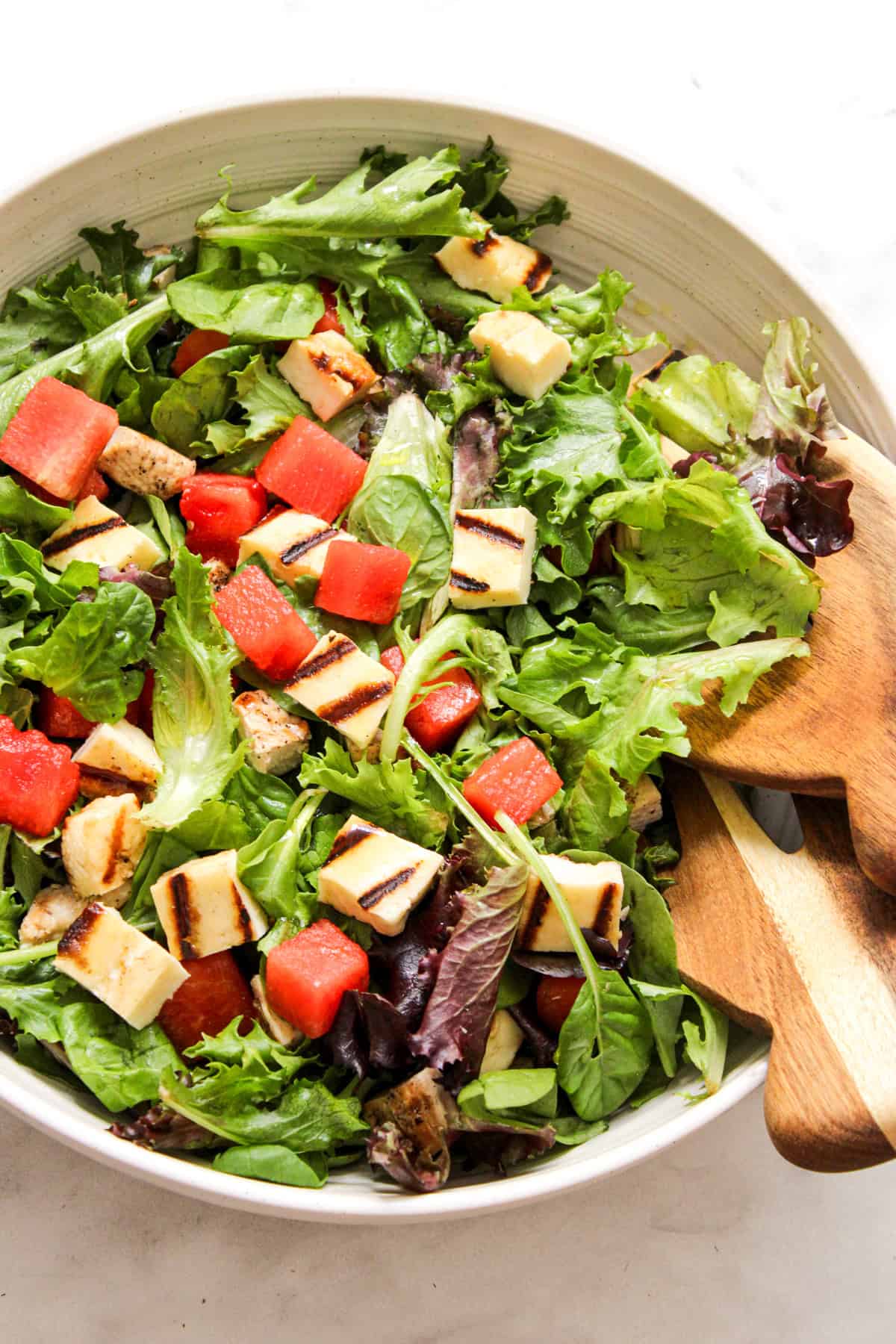 mixed salad in a ceramic bowl with wooden salad tongs resting on the side of the bowl