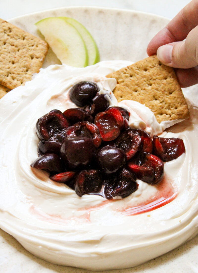 hand holding a graham cracker scooping cherry cheesecake dip