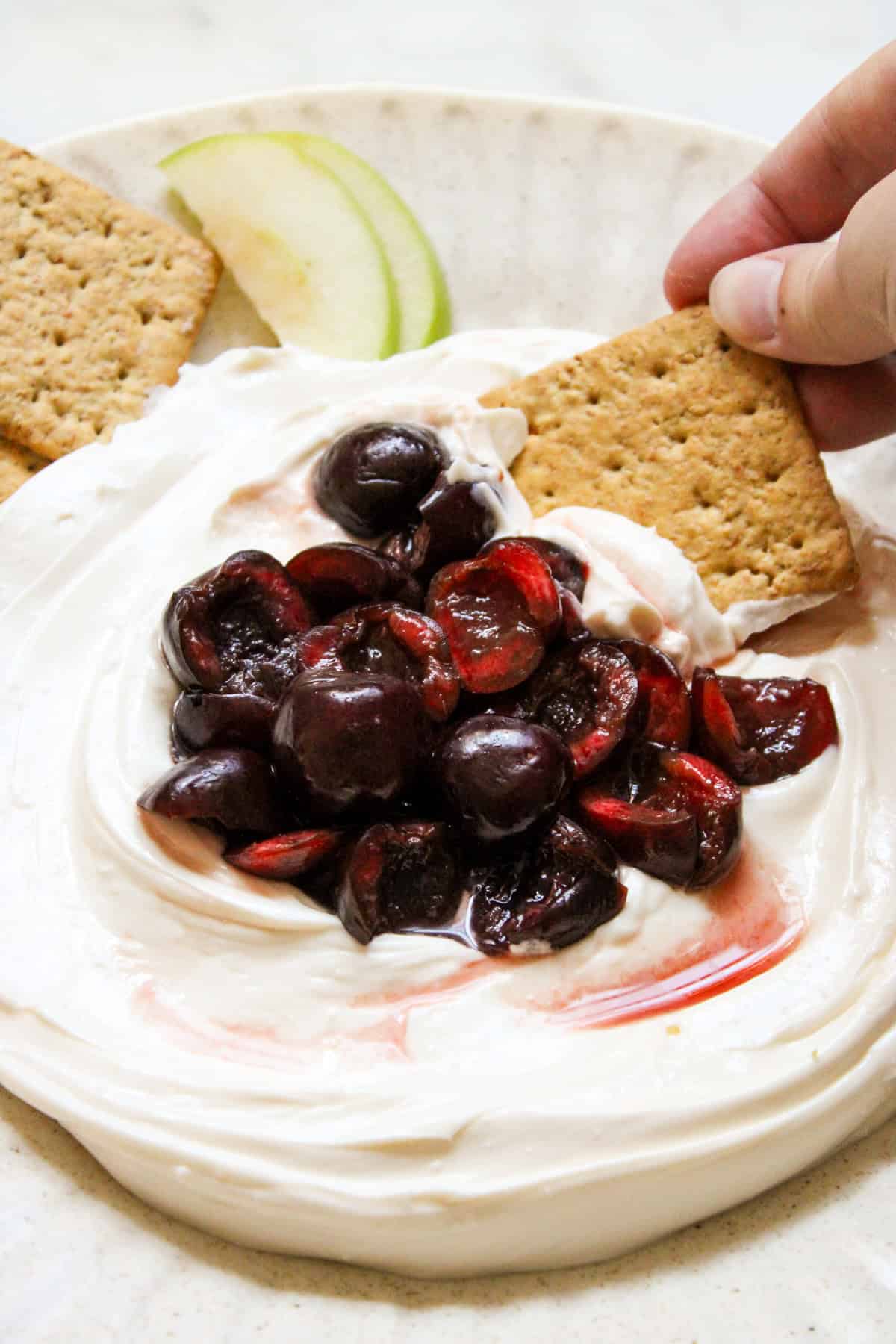 hand holding a graham cracker scooping cherry cheesecake dip