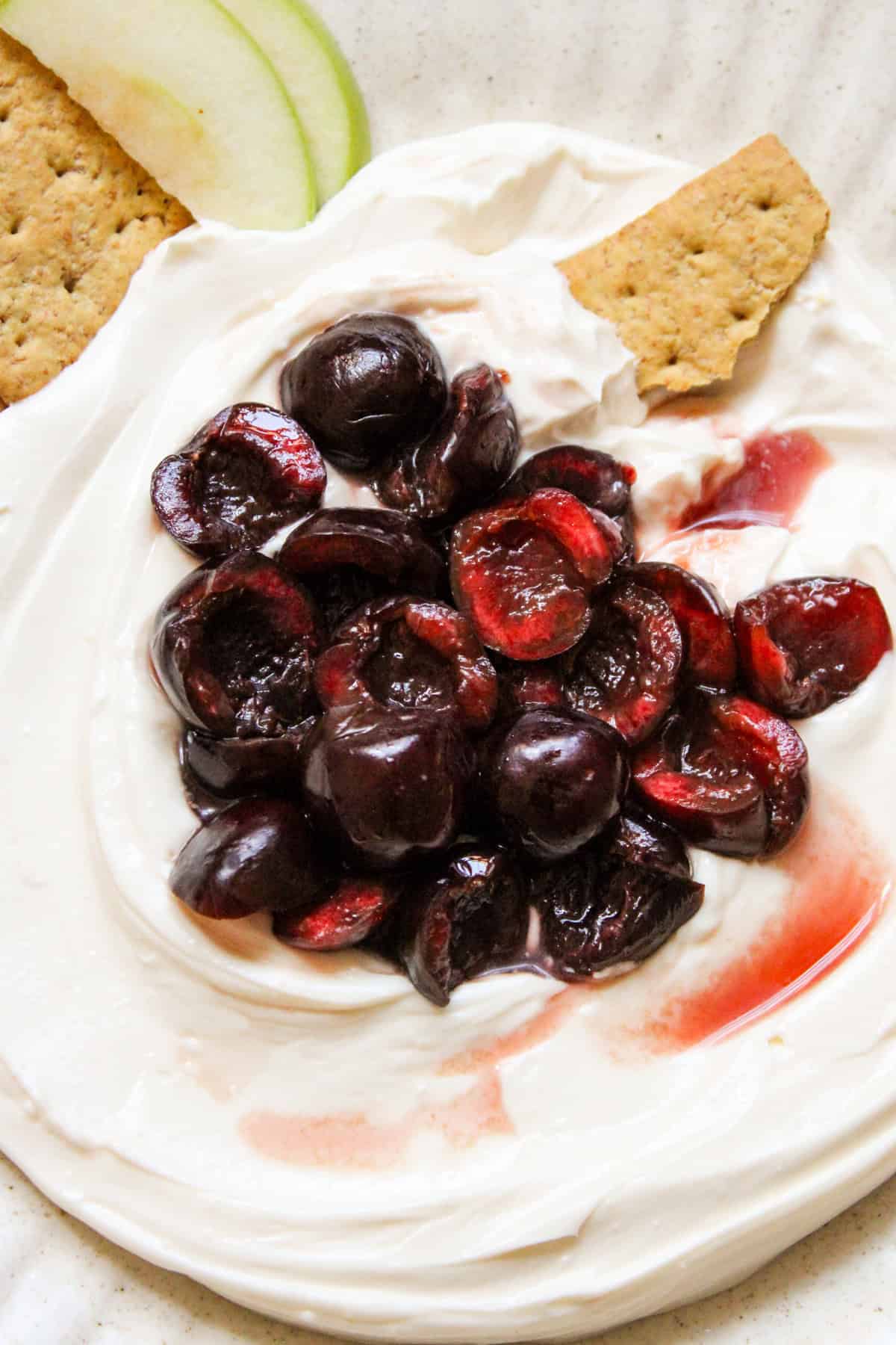 close up shot of juicy pitted cherries on top of cheesecake dip with a broken graham cracker