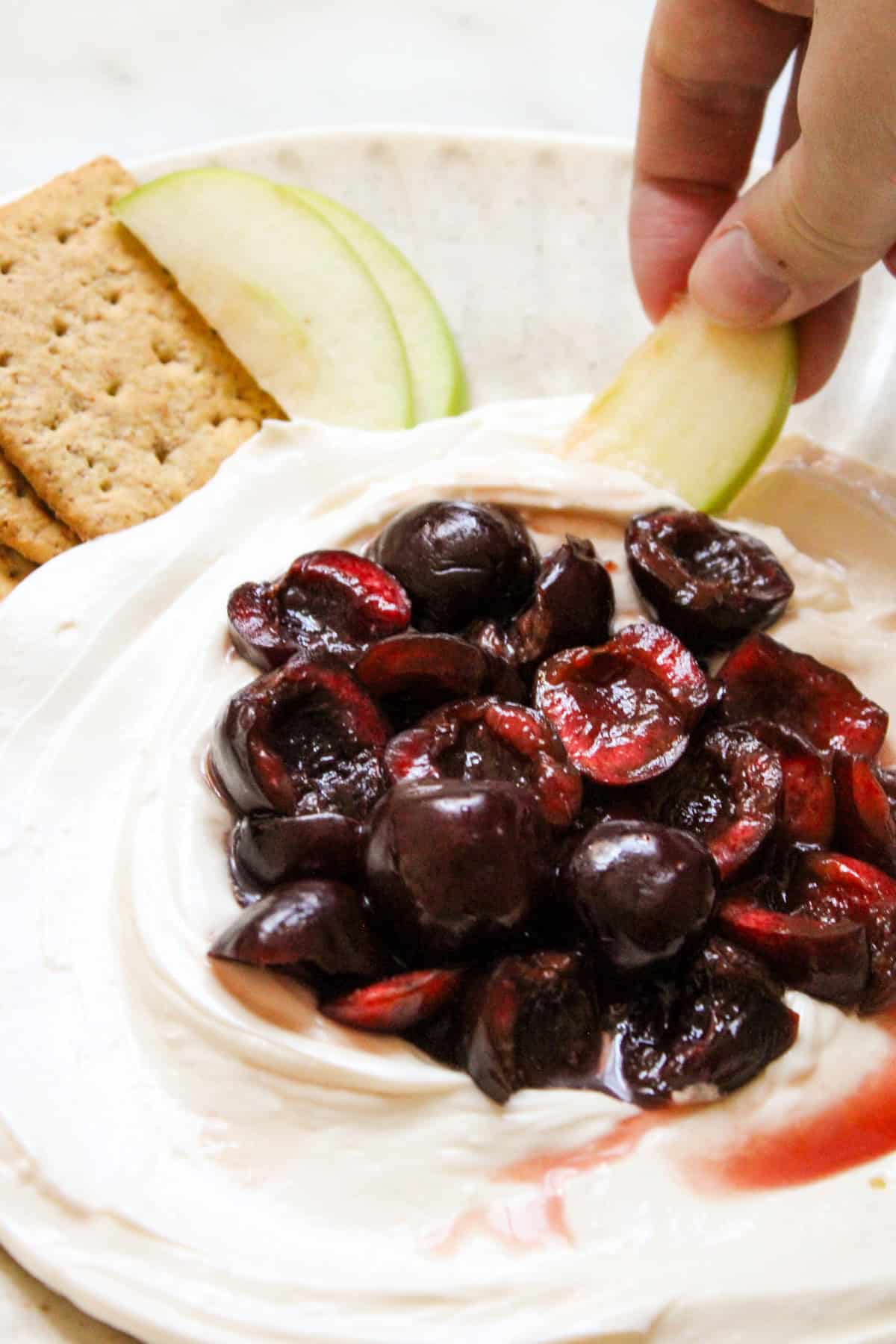 a hand holding a slice of green apple scooping up dip