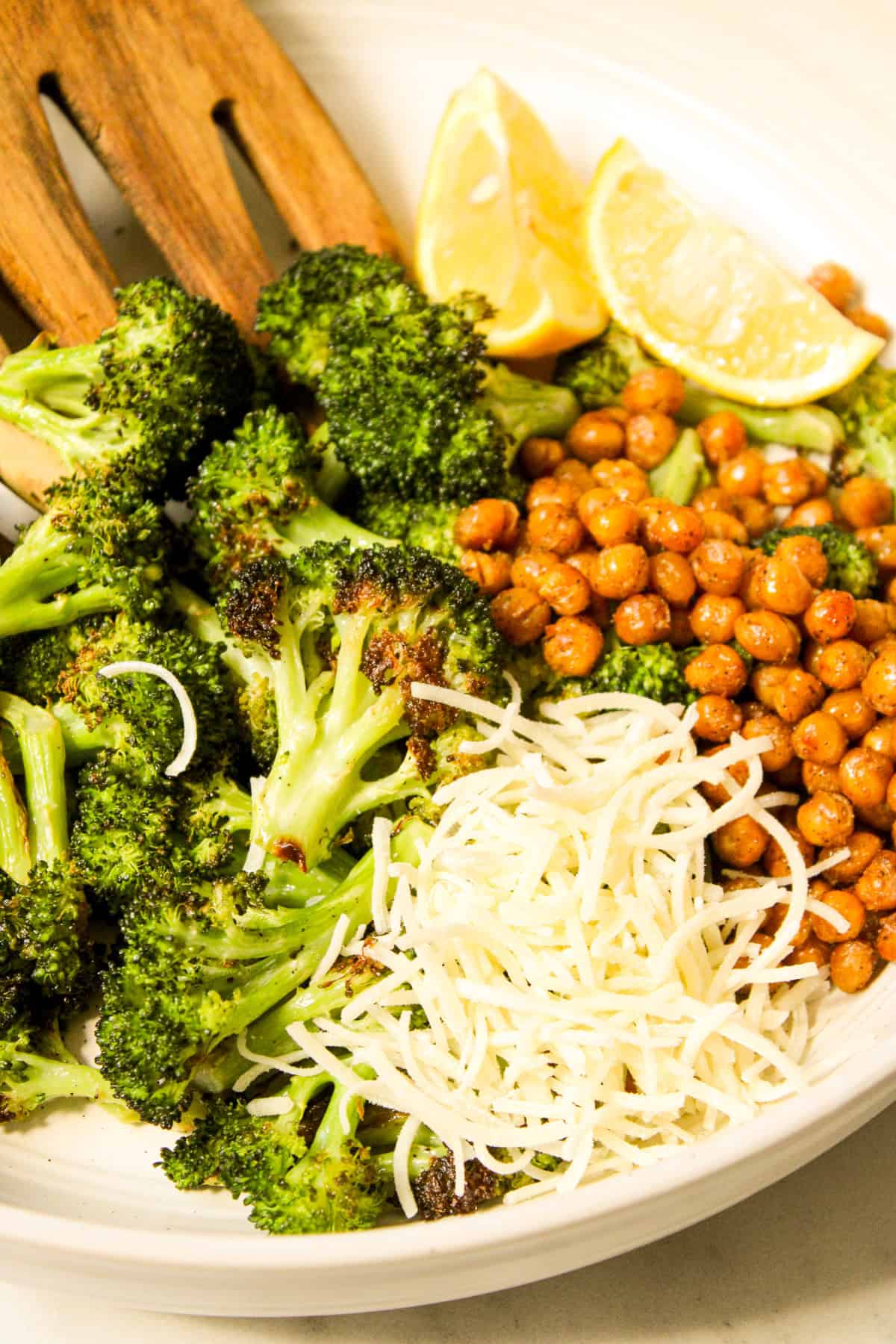 ceramic bowl with roasted broccoli, shredded parmesan, chickpea croutons, lemon wedges and wooden salad tongs